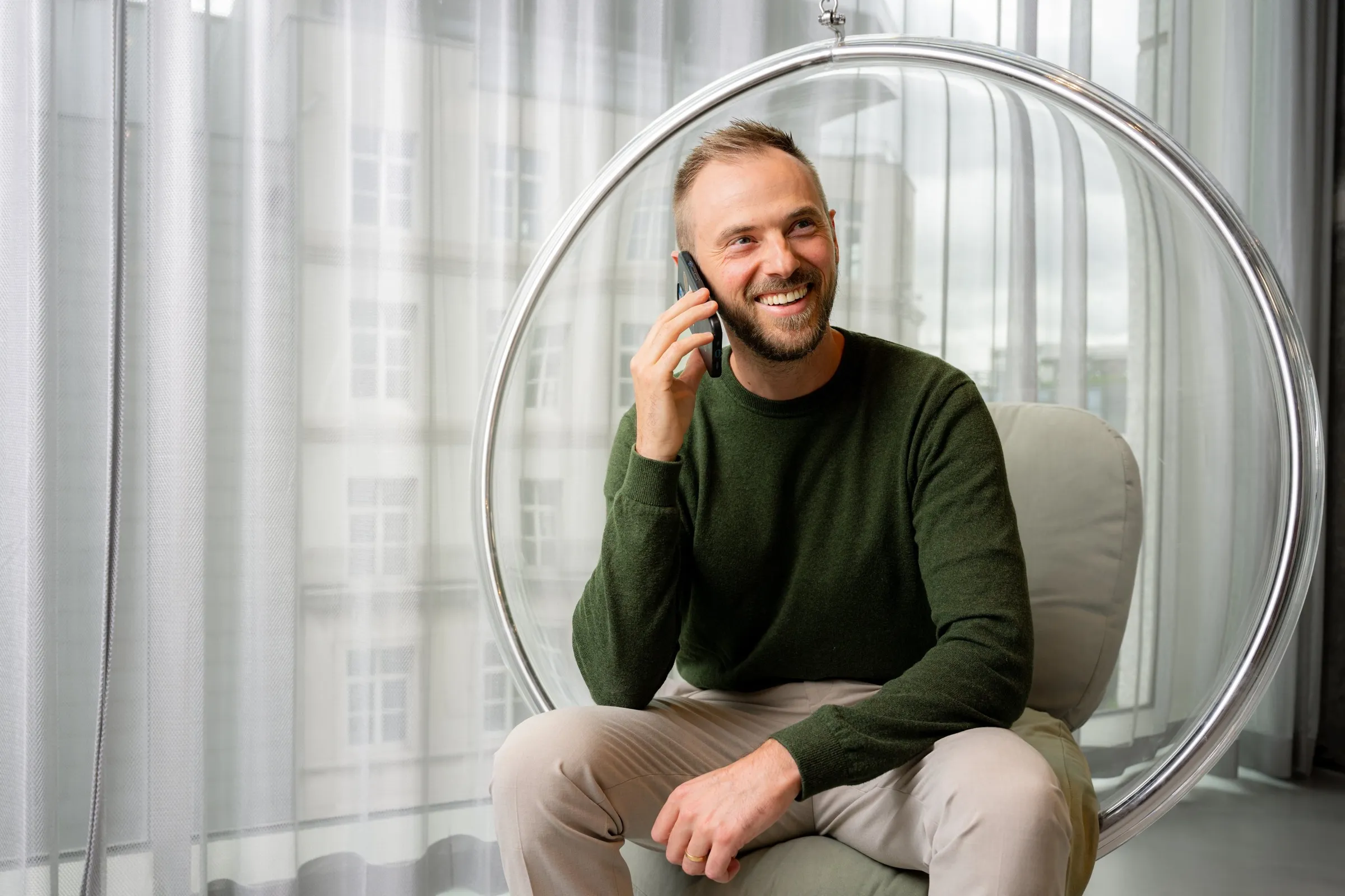 Brecht Vandewaetere lacht tijdens een telefoongesprek, zittend in een hangende bolstoel