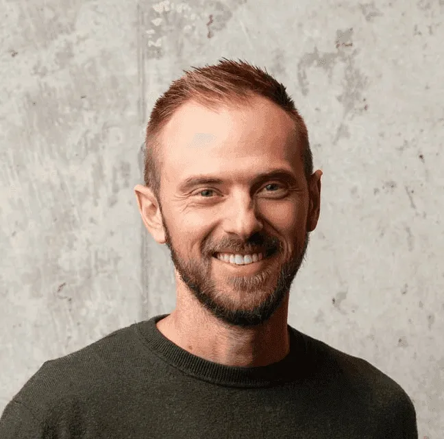 Portret van Brecht Vandewaetere, glimlachend voor een betonnen muur